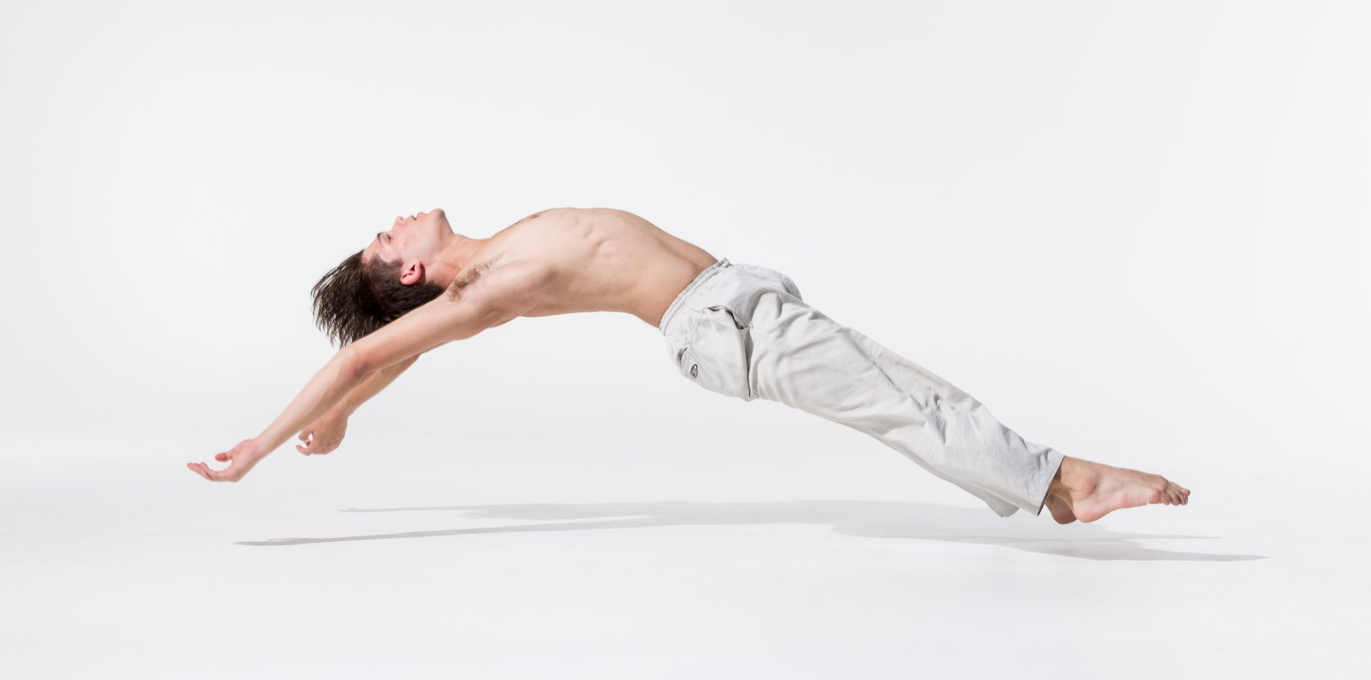 Dancer, Seth Ward, wearing white pants lies back as if floating on a white background.