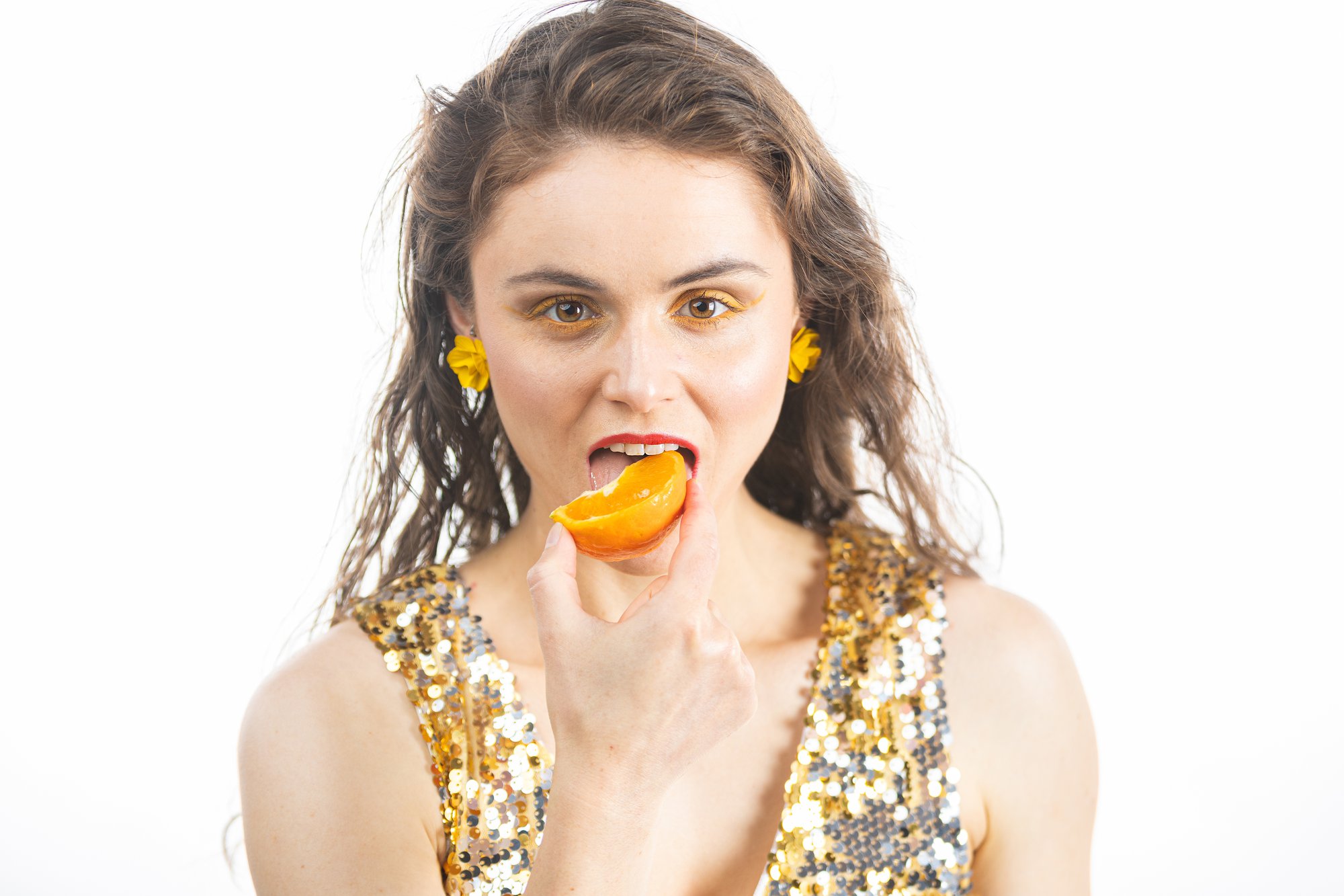 Letitia wearing a gold sequinned top and yellow earrings is eating an orange.jpg