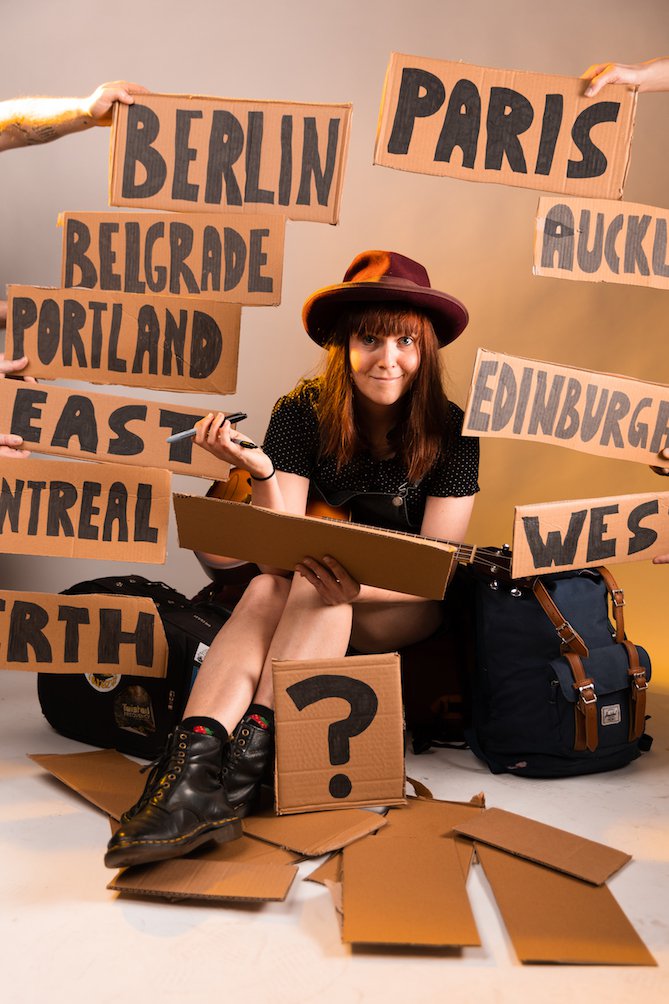 A person surrounded by signs on pieces of cardboard with the names of cities on them.